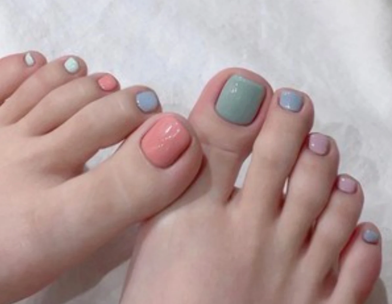Pedicure with each toe in a different pastel — sage, coral, periwinkle and lilac